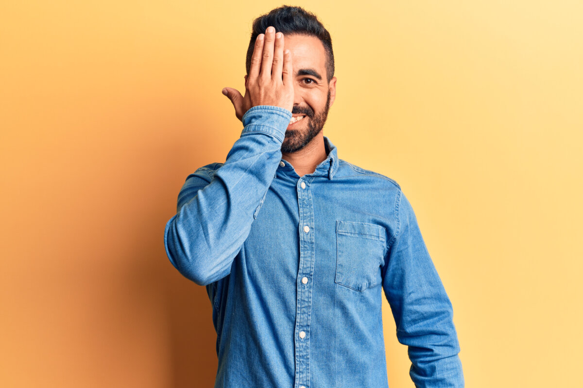 man wearing casual clothes covering one eye with hand