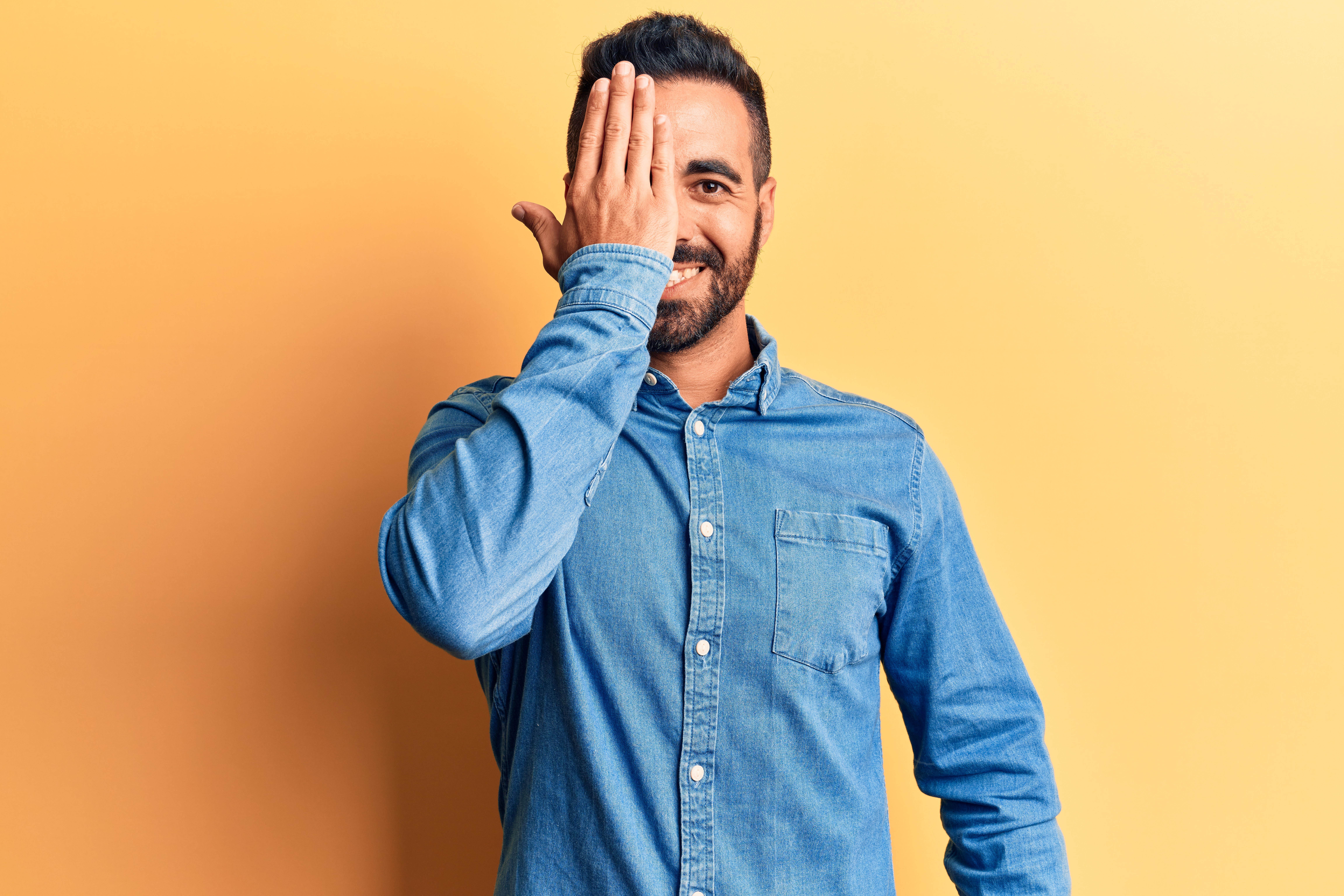 man wearing casual clothes covering one eye with hand