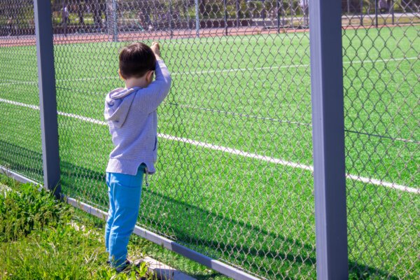 child alone looking at a football stadium from behind fence