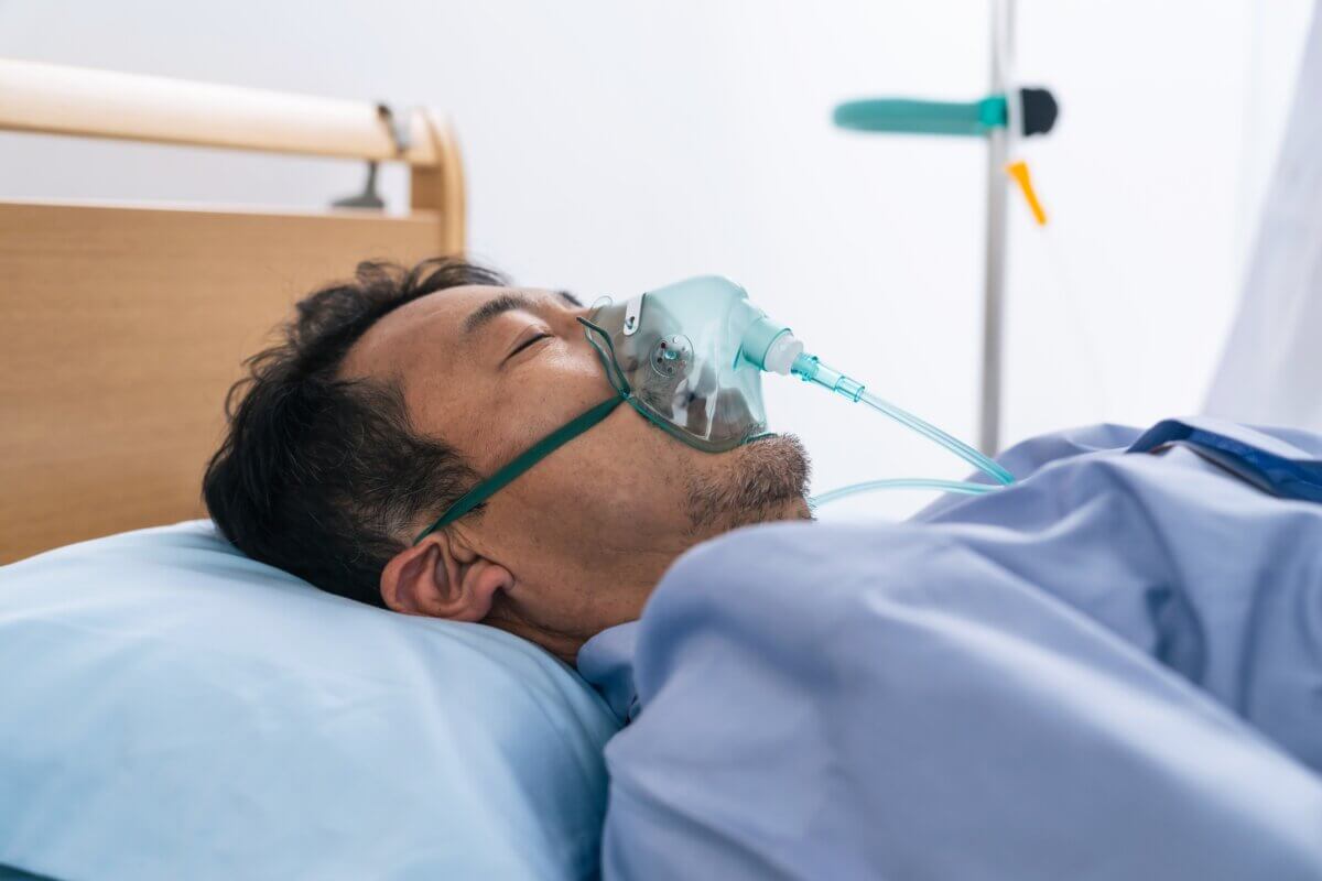 A middle-aged male patient in a coma in a hospital bed.