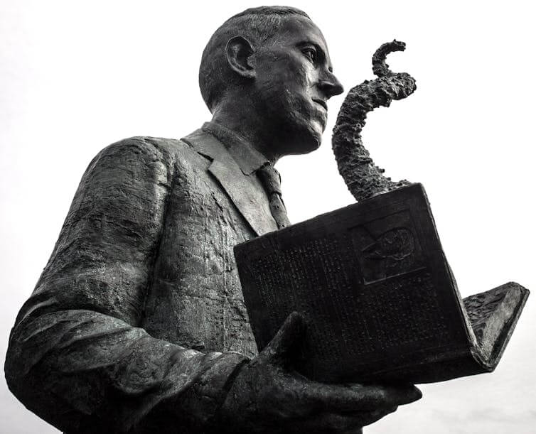 Statue of young man wearing a suit and holding an open book with a tentacle emerging from the pages of the book.
