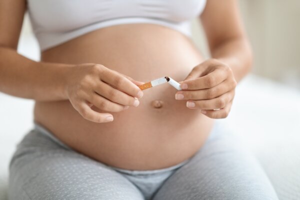pregnant woman sitting on bed at home, breaking cigarette