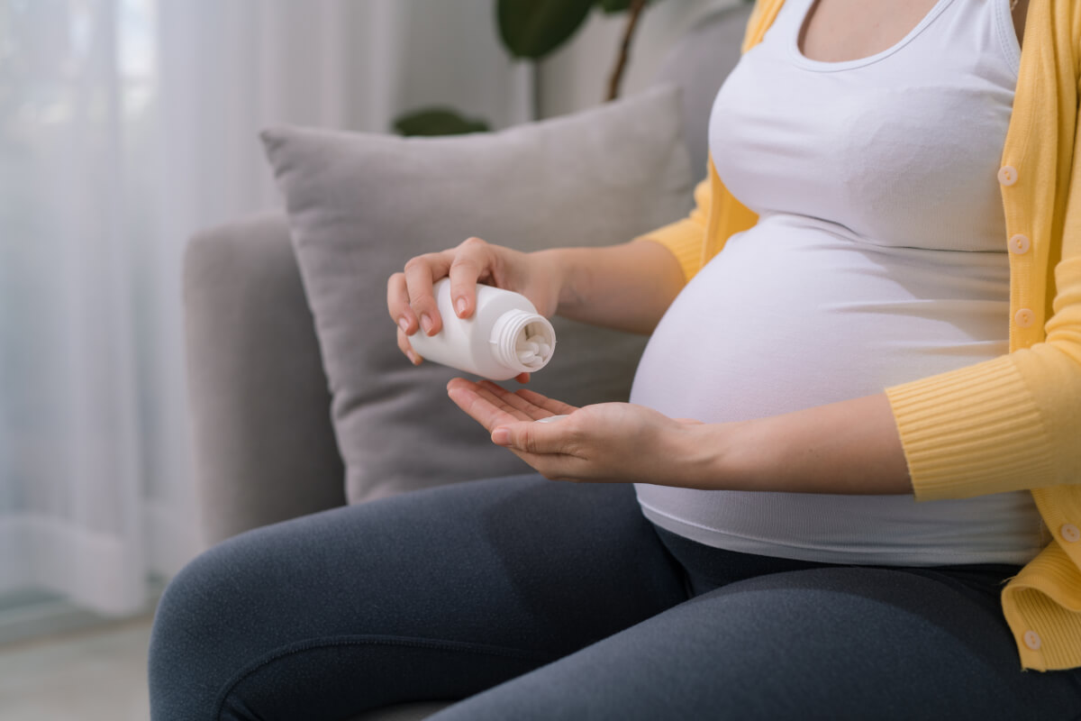 Pregnant woman holding plastic jar with pills