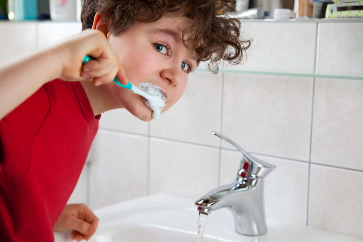 Kid brushing teeth with sink running