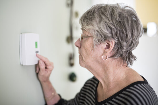 Older woman adjusting the thermostat setting in her home