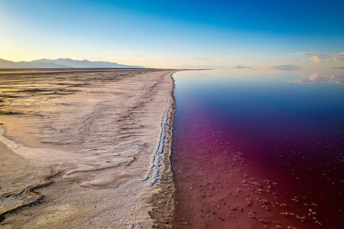 Aerial view of the Great Salt Lake in Utah with a striking contrast between the salt flats and the vibrant pink water under a clear blue sky.