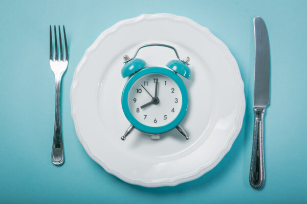 An alarm clock sits on a plate to signify intermittent fasting