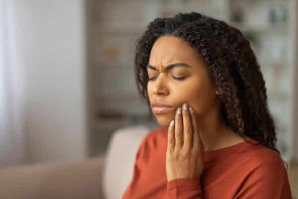 Woman holds her hand over a toothache, possibly a cavity or dental issue