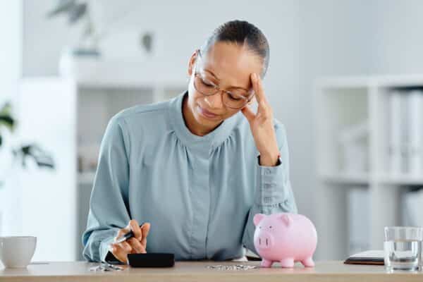 A woman stressed about her finances calculating her budget with a piggy bank