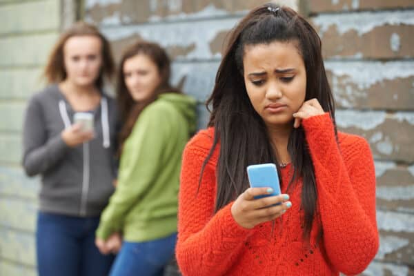 A girl worried on her cellphone with other teens looking at her in the background