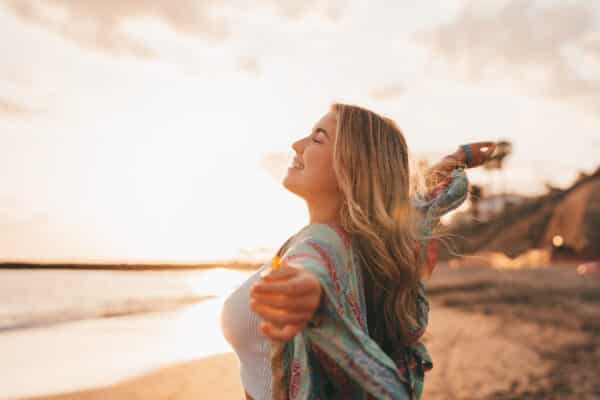 Woman at the beach with open arms enjoying free time and freedom outdoors. Having fun, relaxing, and living happy moments.