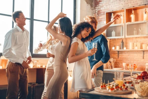 Group of men and women party together dancing inside for friends gathering at home