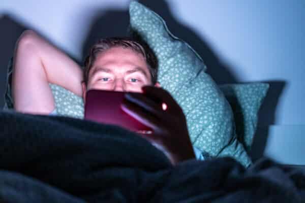Man using his smartphone in bed with high level of blue light exposure