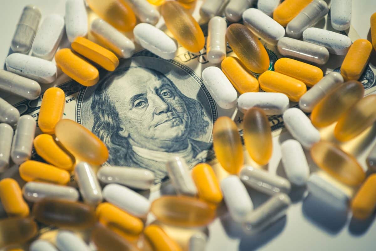 A one-hundred dollar bill surrounded by pills and prescription drugs, signifying "big pharmacy."