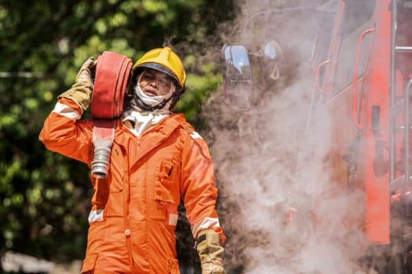 Firefighter carries a hose while smoke rises