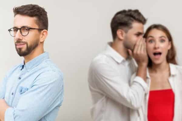 A man smiling while two people gossip about him