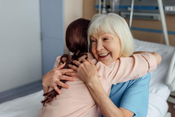 Older woman in hospital hugging a family member from bed