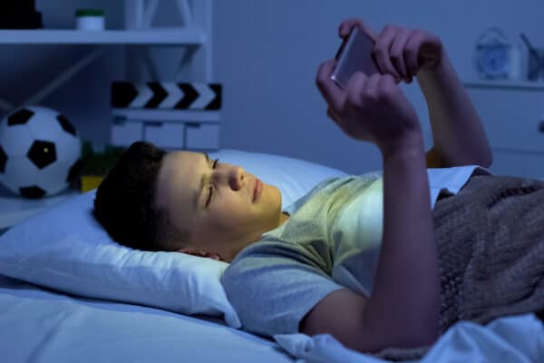 Teenager watching smartphone screen in bed