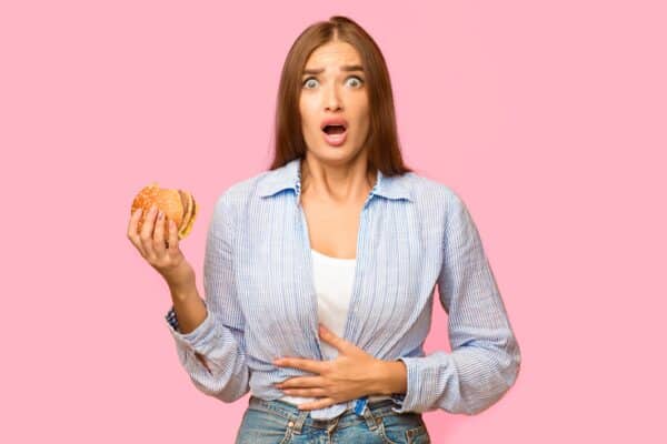 A woman with a stomach ache holding a burger