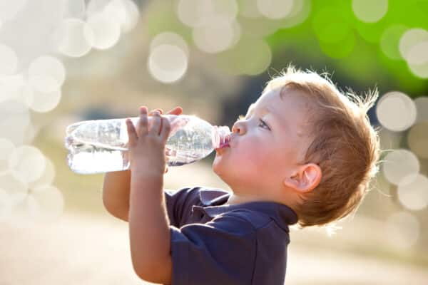 Boy drinking bottled water outside on hot summer day
