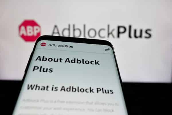 Mobile phone with website of ad blocking company Adblock Plus on screen in front of logo.