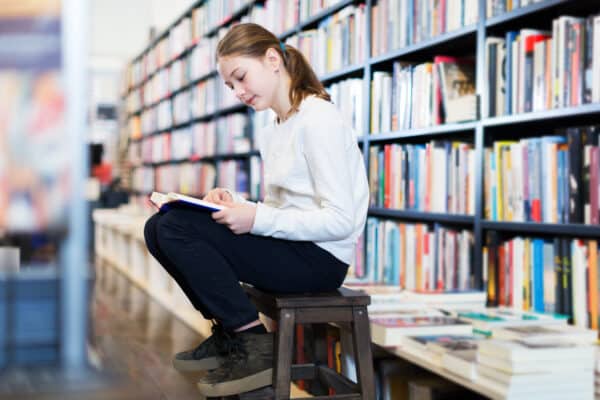 Teen girl reading book in library or store