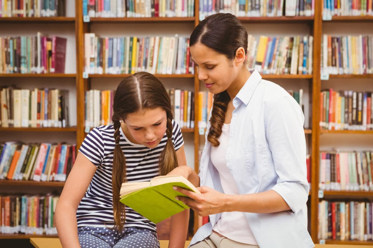 Librarian showing book to young teen girl at school library