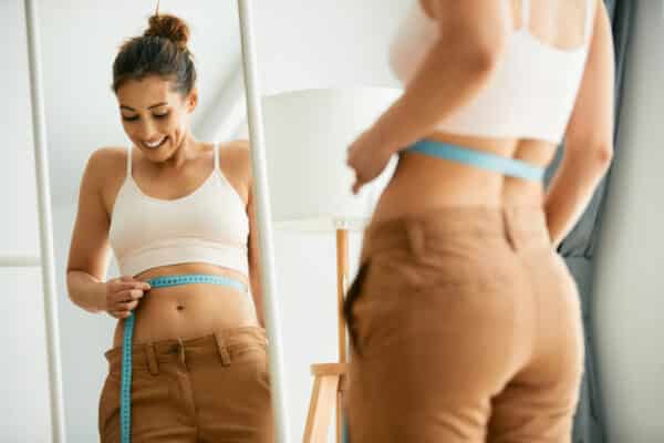 Woman measuring her waist size in the mirror