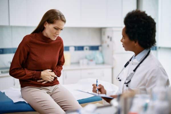 Female patient holding her abdomen in pain while talking to her doctor.