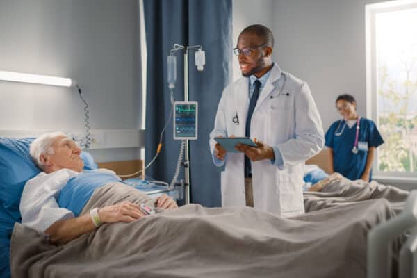 A doctor speaks to an elderly patient in a hospital bed