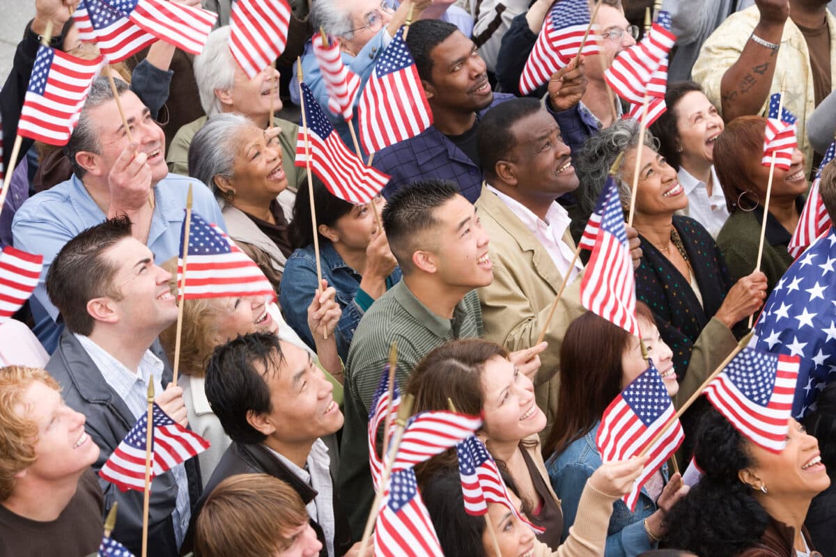 A crowd of diverse and multicultural Americans waving flags to celebrate the United States.
