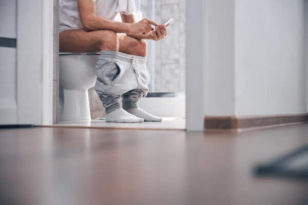 Man using his smartphone while sitting on the toilet