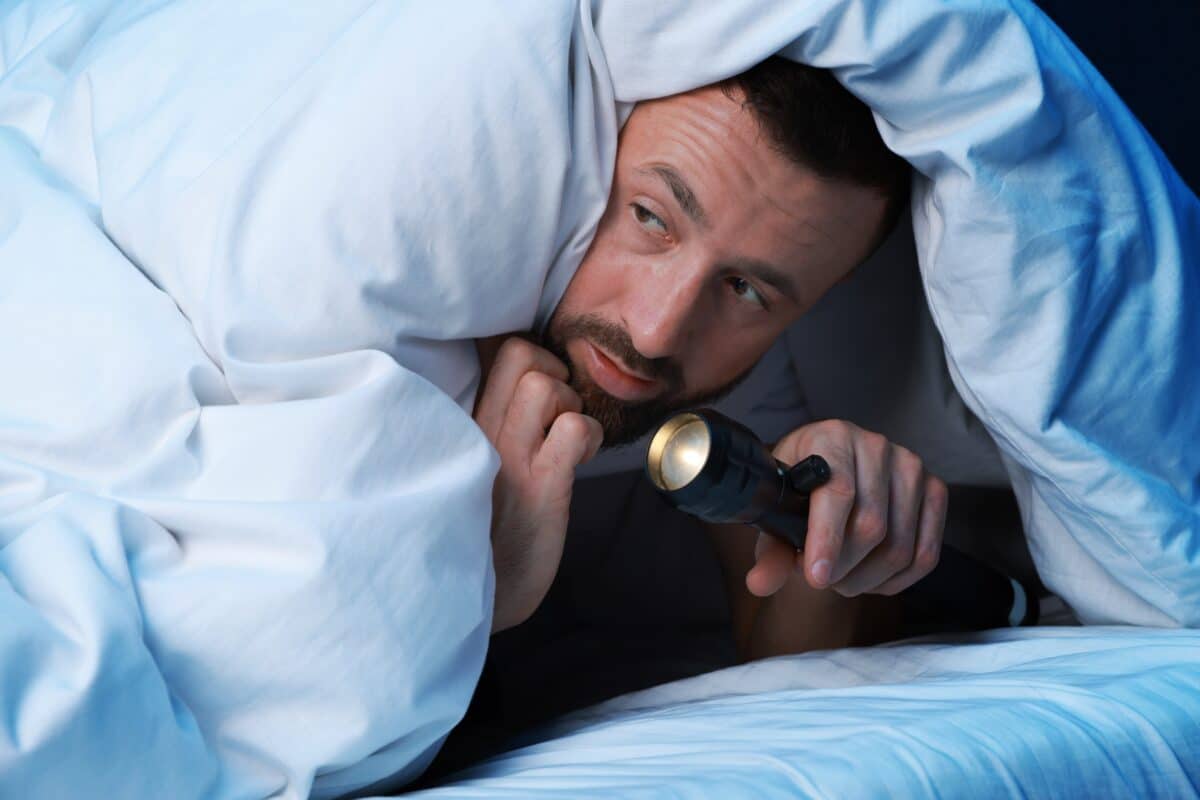 Man hides under his covers with a flashlight afraid of the dark
