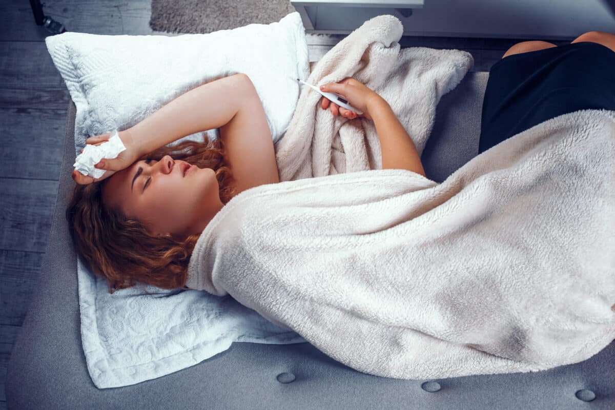Sick woman in bed with a thermometer