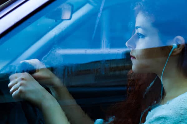 Young woman or teen driving while listening to music or ear buds