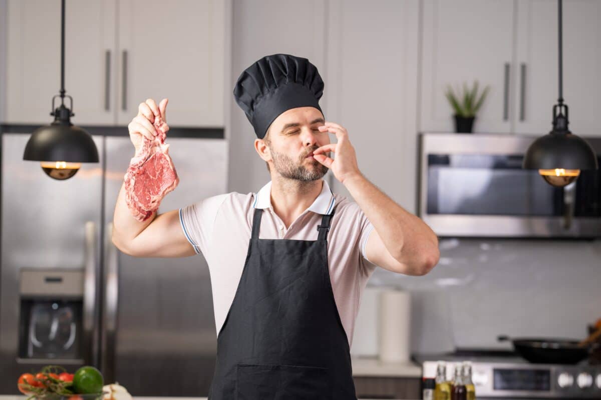 A chef holds a piece of steak and kisses his fingers