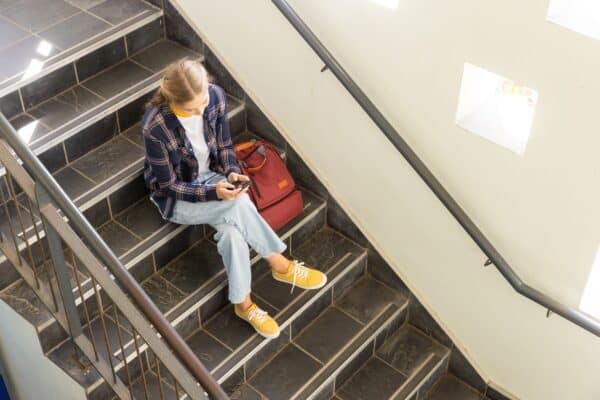 Teen student sitting using smartphone in school hallway