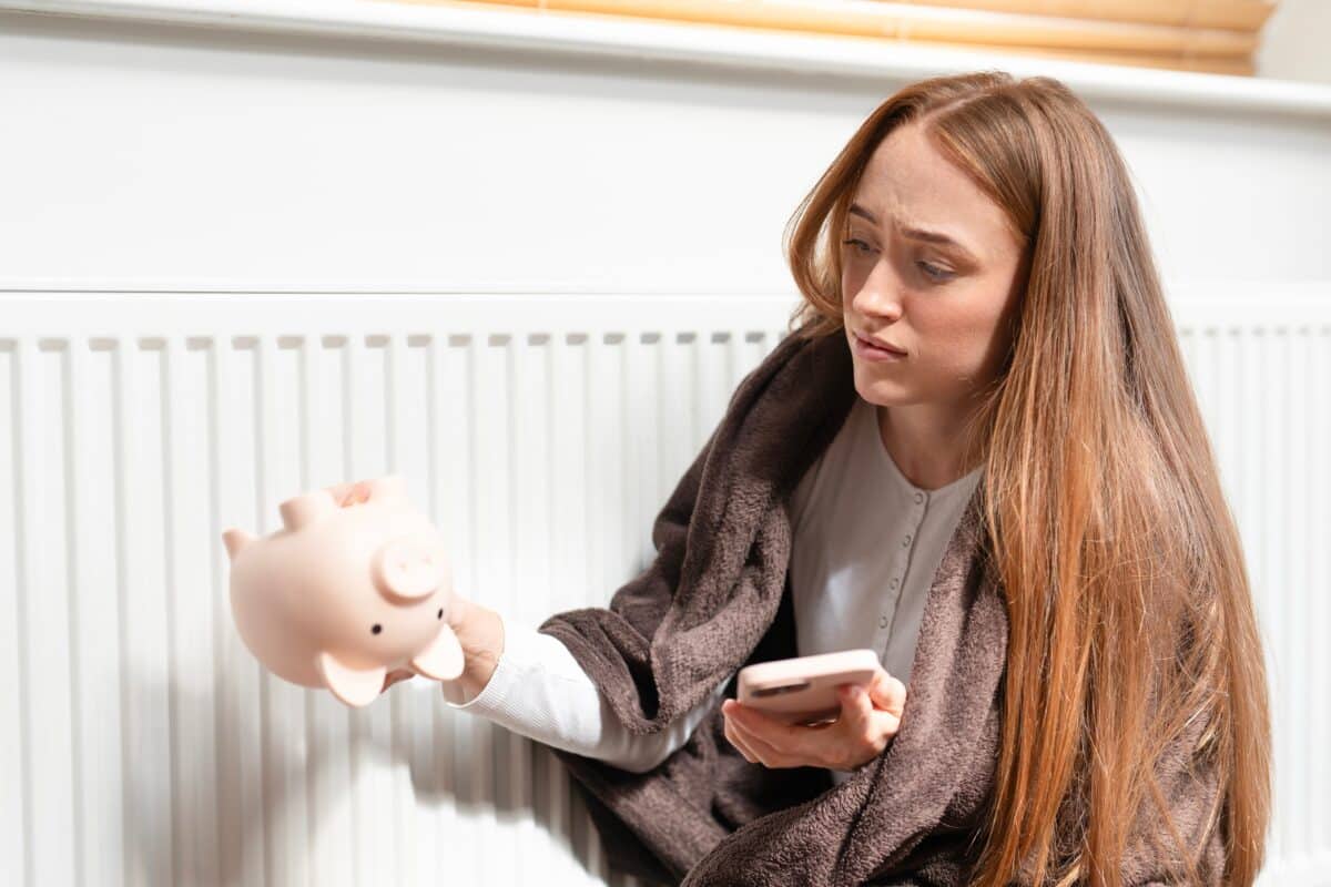 Concerned,Woman,Checks,Phone,While,Examining,Empty,Piggy,Bank,Near