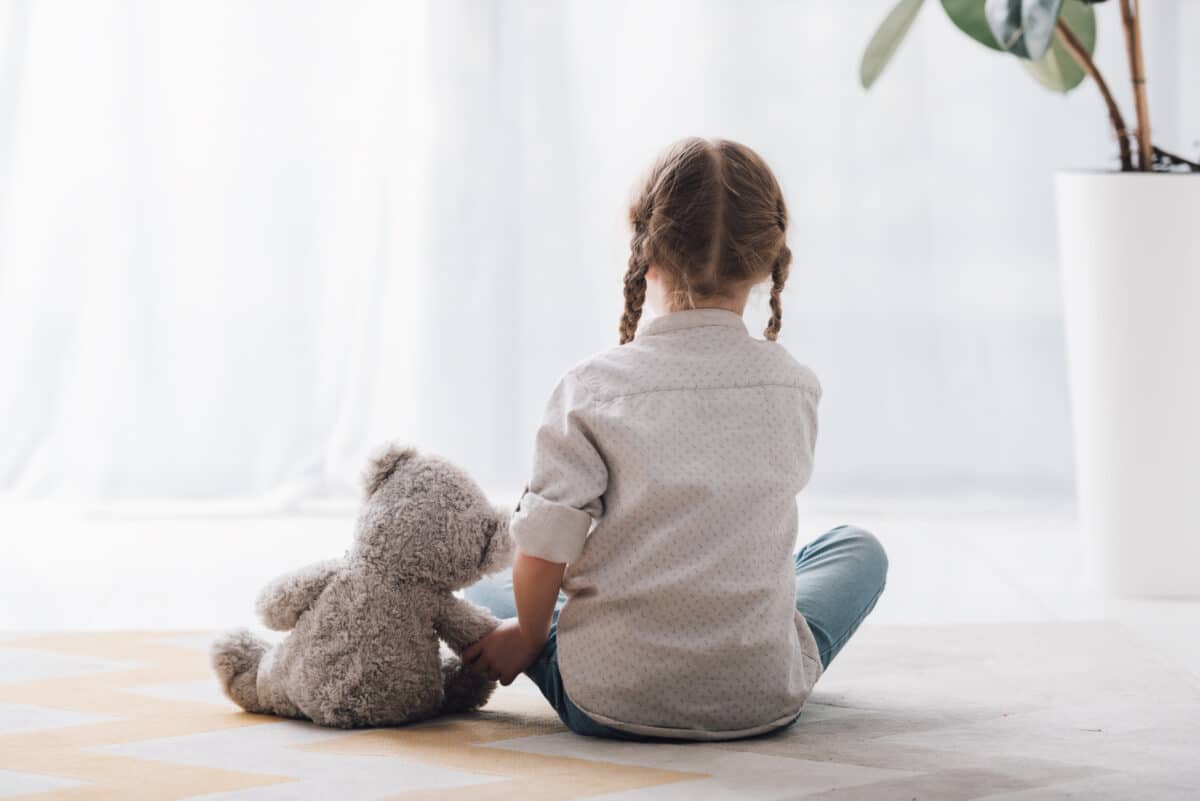 A young child sits with her teddy bear