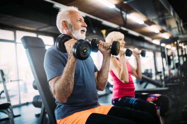 Two older adults exercings at a gym while sitting and holding hand weights