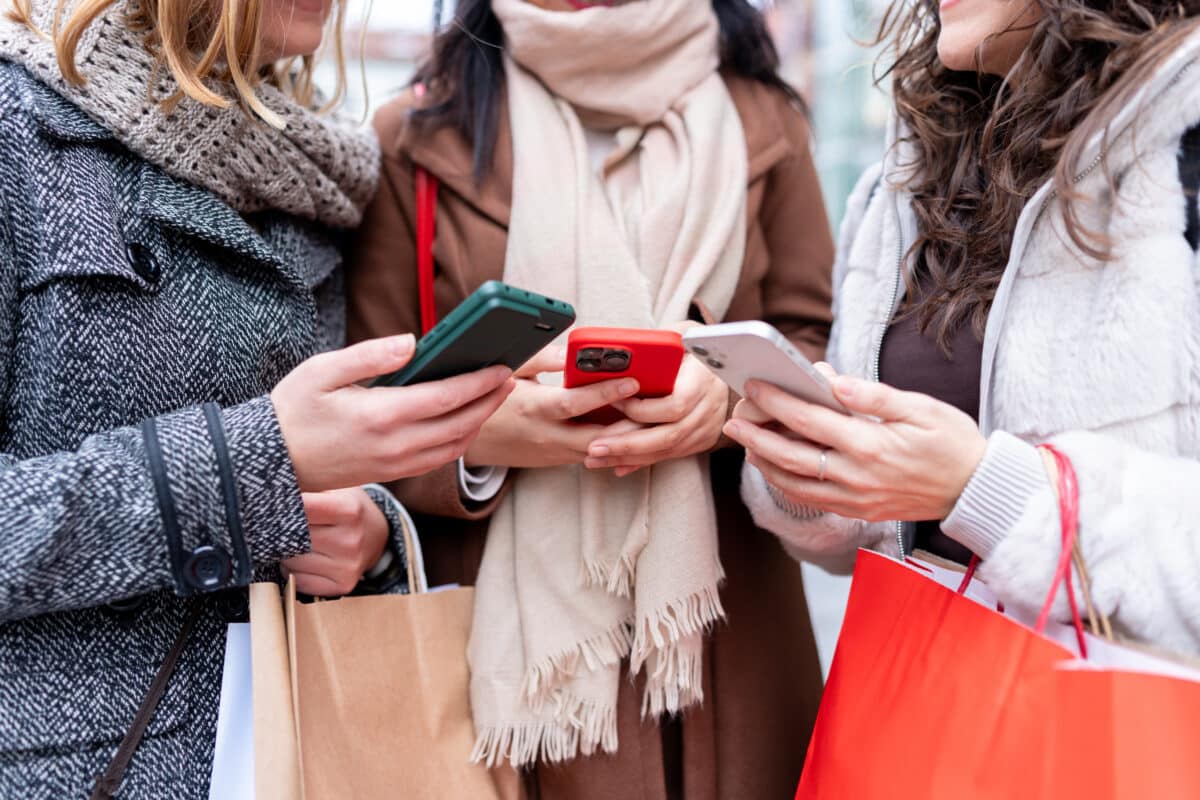 Women friends using smartphones shopping in city