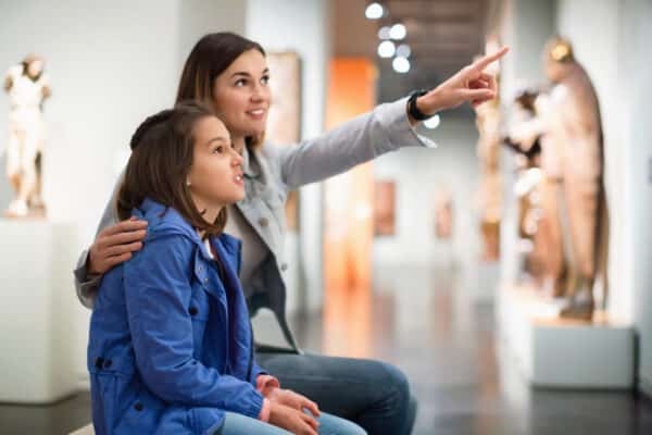 Smiling pleasant cheerful mother and daughter regarding ancient statues in museum