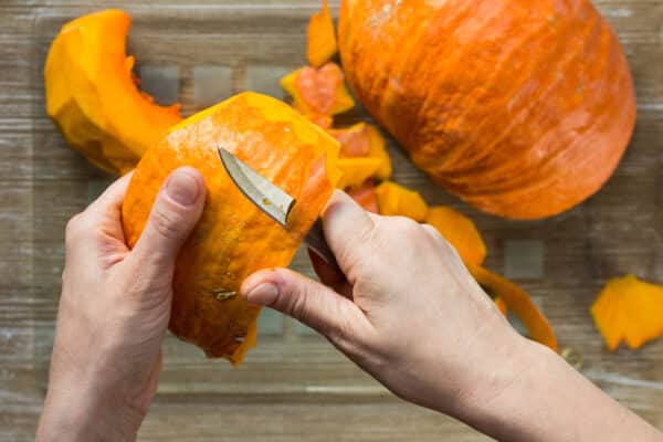 Peeling off pumpkin with ordinary knife by woman hand on wooden background