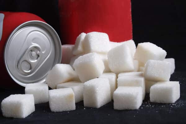 Unhealthy diet concept: A large pile of white sugar cubes next to generic red soda cans representing high calorie and sugar content in soft drinks