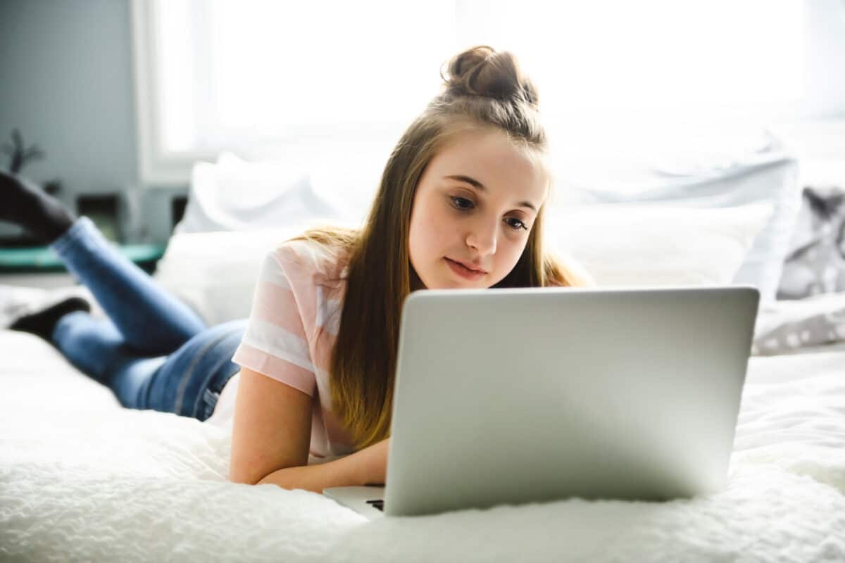A Young smiling teen girl on bed with laptop