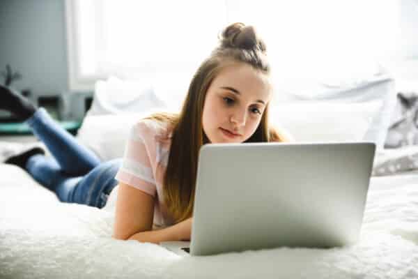 Young smiling teen girl on bed with laptop