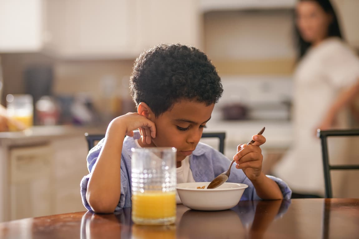 cute little boy eating breakfast with mother behind him