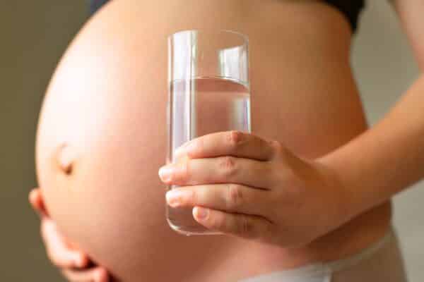 pregnant woman holding her belly and a glass water in the hand