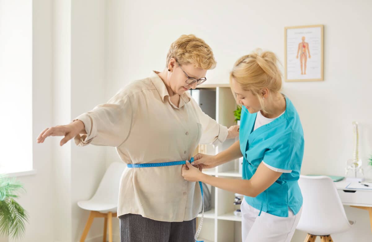Nurse measuring waist of senior woman patient during visit in clinic
