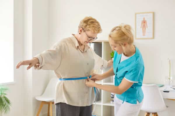 Nurse measuring waist of senior woman patient during doctor visit